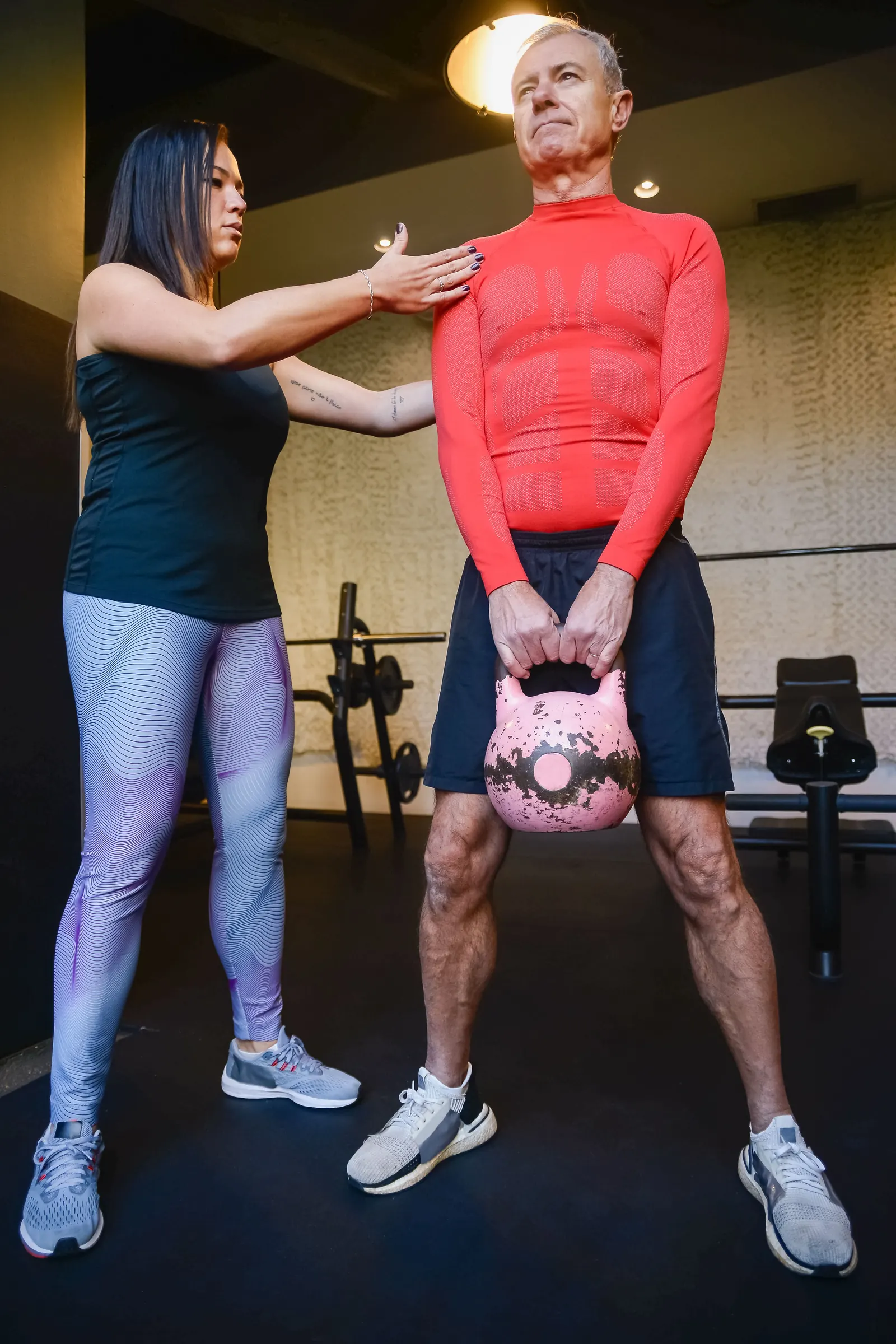 Een trainster corrigeert de houding van een man die een kettlebell optilt